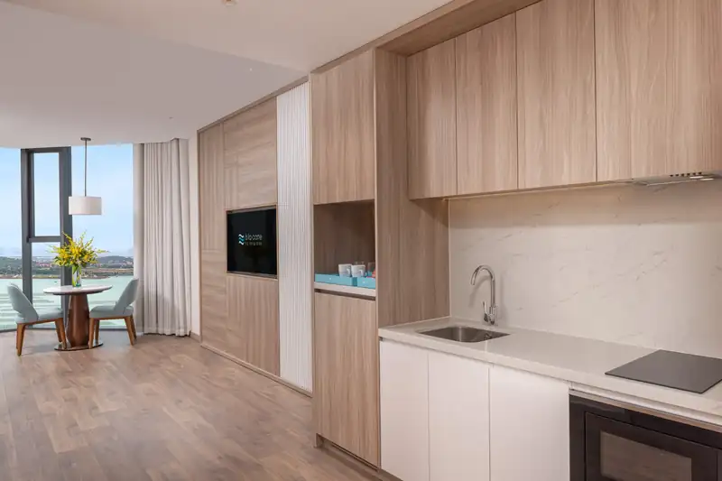 Góc bếp nhỏ có bếp từ, bồn rửa và bàn tròn sát cửa kính trong phòng Executive Bay View