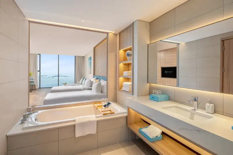 Bồn tắm và bồn rửa đá, nhìn xuyên vách kính ra giường và vịnh trong phòng Premier Bay View
