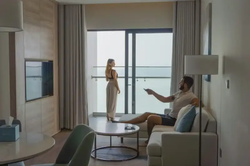 Khách ngồi phòng khách Suite Bay Vista, cửa kính mở ra ban công nhìn vịnh